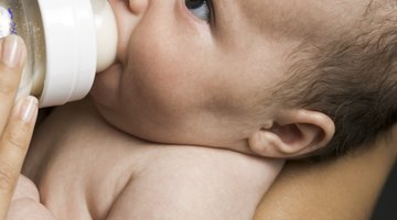 Mother Feeding Baby Sitting In High Chair At Mealtime