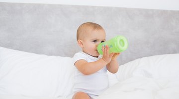 Little baby with bottle in white bed
