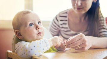 Person spoon feeding baby in high chair