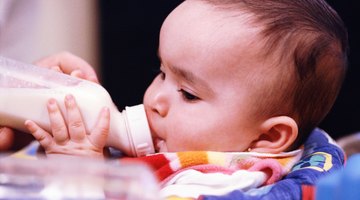 A caucasian older sister bottle feeds her little baby brother