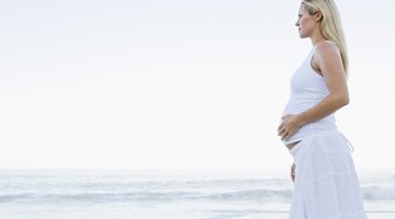 Daughter listening to pregnant mid adult mothers belly, smiling