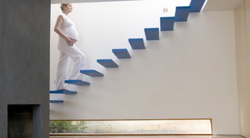 Beautiful pregnant woman sitting at bed and holds hands on belly in bedroom at home.