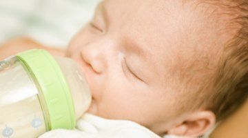 Mother Holding Newborn Baby Daughter At Kitchen Table