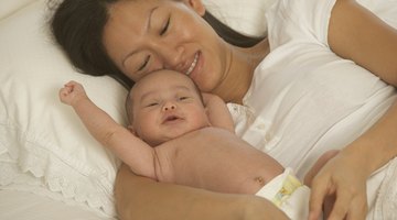 side view of a mother lying on a bed holding her baby (6-12 months)