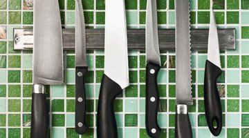 Stainless steel knives hang on a magnet in a kitchen.
