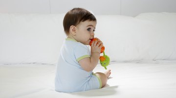 Baby girl (15-18 months) sitting on bed, biting toy