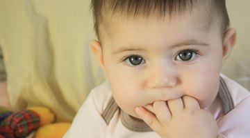 Baby girl (15-18 months) sitting on bed, biting toy