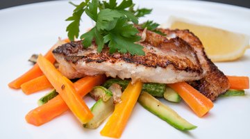 person using a fork and knife on a plate of grilled salmon