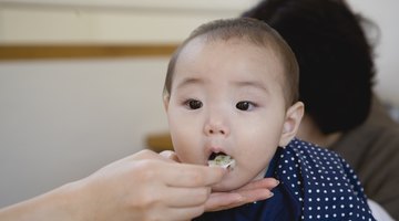 Person spoon feeding baby in high chair