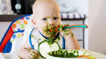 Mother Feeding Baby Sitting In High Chair At Mealtime