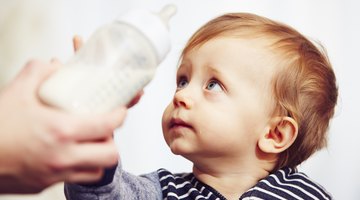 Baby boy drinking milk from a bottle in sunny nursery