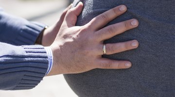 Three women sitting on sofa, two feeling pregnant woman's bump