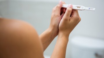 close-up of a young woman crossing her fingers while looking at a pregnancy test