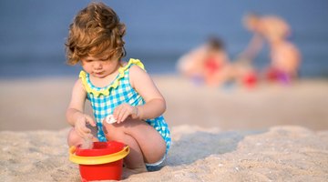 A child plays in the sand with a pail, not a bucket.
