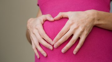 Pregnant woman is standing on the green lawn.