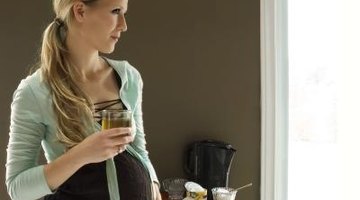 Pregnant woman drinking glass of water in kitchen at home.
