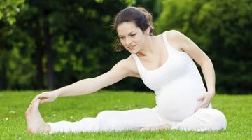 Pregnant woman is standing on the green lawn.