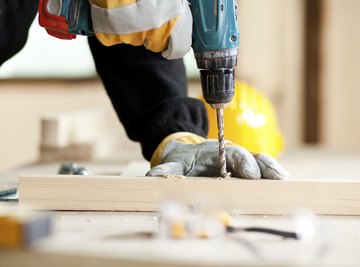 A close-up of a carpenter drilling a hole with a drill bit.