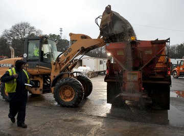 A front end loader dumping salt and sand into the back of a dump truck.