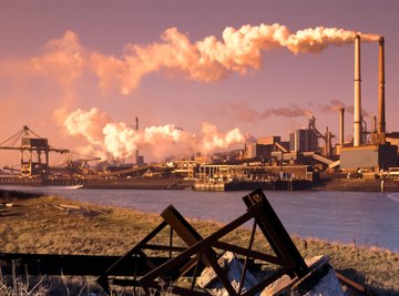 Steel factory along a body of water shoots out smoke from its chimneys.