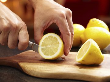 Hand slicing lemons on cutting board.