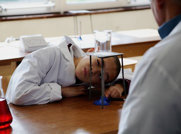 A boy heating up a beaker of water on a bunsen burner in a science room.