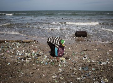 A man collecting trash that has washed up on the beach.