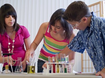 A teacher watching students looking at test tubes during a science fair.