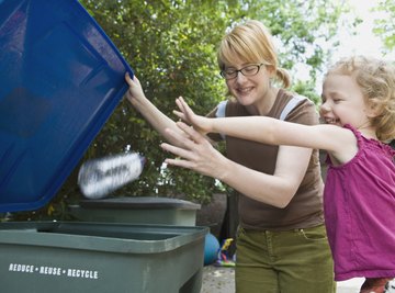 Two siblings tossing a plastic bottle into a recycling bin.