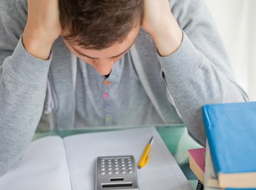 A student looks down at an empty notebook and a calculator on his desk.