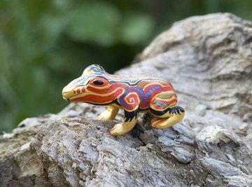 A painted clay frog sits on a log outside.
