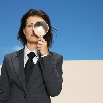 businesswoman in desert holding magnifying glass, portrait