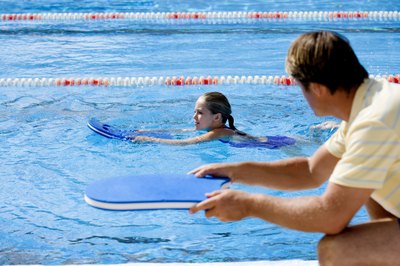 Polka Dot Images/Polka Dot/Getty Images Practice flutter kicks with a kick board.