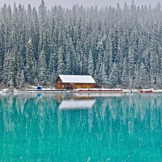 Cabin in the woods in front of a lake with snow all around.