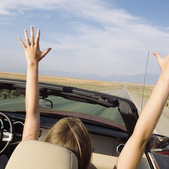 Woman with hands in her air rides in a convertible.
