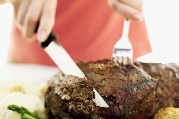 Close-up of a woman's hands slicing roast beef with a knife