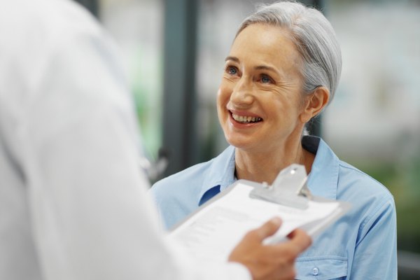 Close-up of doctor talking to mature patient while holding clipboard