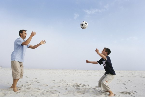 Father and son (12-13 years) playing with ball on beach, side view