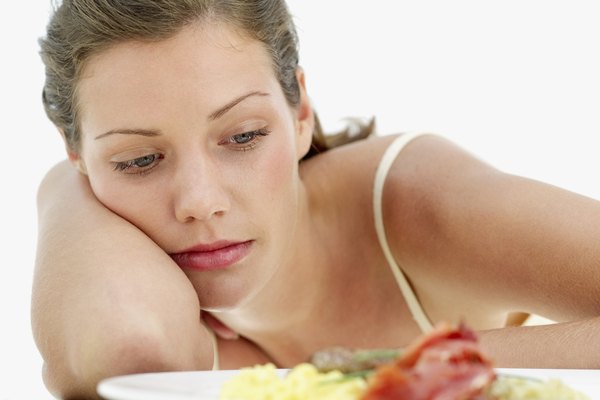 close-up of a young woman leaning on a table in front of a plate of scrambled eggs with bacon and sausages