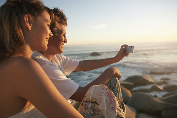 Teenage couple (15-19) on beach, boy taking photograph