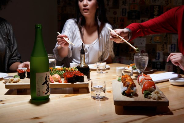 Three young women eating sushi in restaurant, mid section