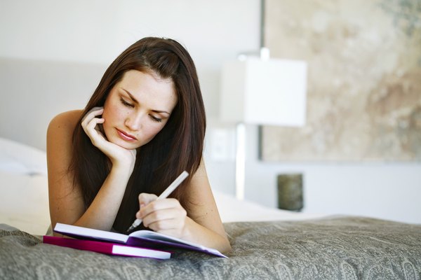 Young woman lying on a bed writing in a notebook