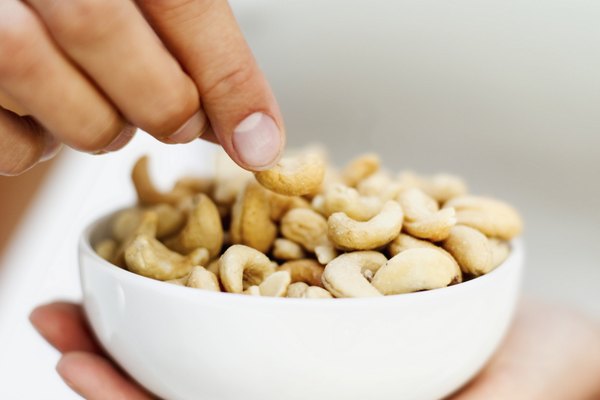 Close-up of a man's hand picking a cashew nut from a bowl