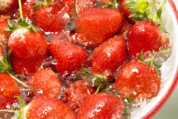 Strawberries being washed in bowl, close up, white background