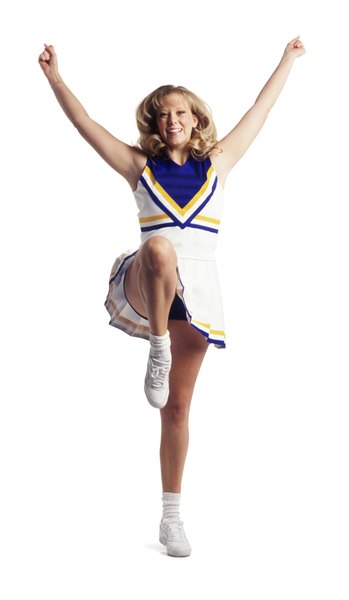a cute teenage female cheerleader throws up her arms and kicks while performing