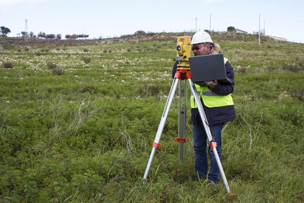 An engineer uses a theodolite on a grassy field