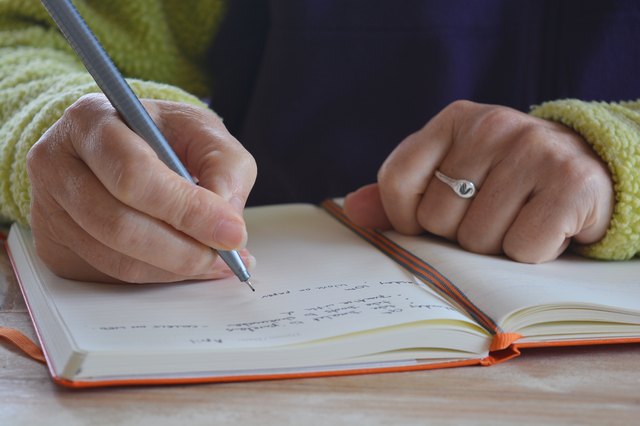 Midsection Of Woman Writing On Book While Sitting At Table In Home