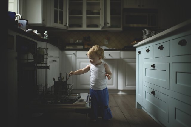 Cute baby girl holding kitchen utensils while standing in kitchen at home