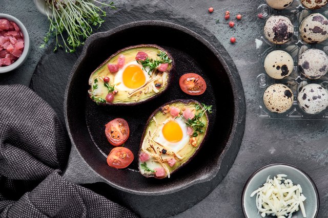 Keto diet dish: Avocado boats with ham cubes, quail eggs, cheese, ingredients around