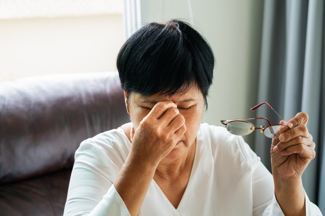 女人去掉眼镜,按摩眼睛在阅读纸质书。感觉不舒服,因为长期戴眼镜,患有眩晕